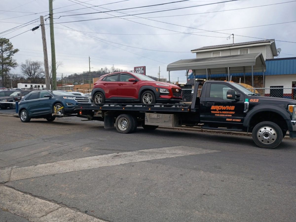 Brown's rollback carrying a red SUV on its deck with a blue SUV lifted behind it.