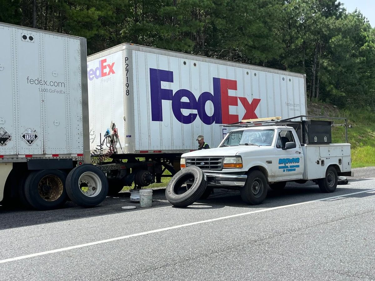Brown's service truck parked beside trailers during tire work on a highway shoulder.